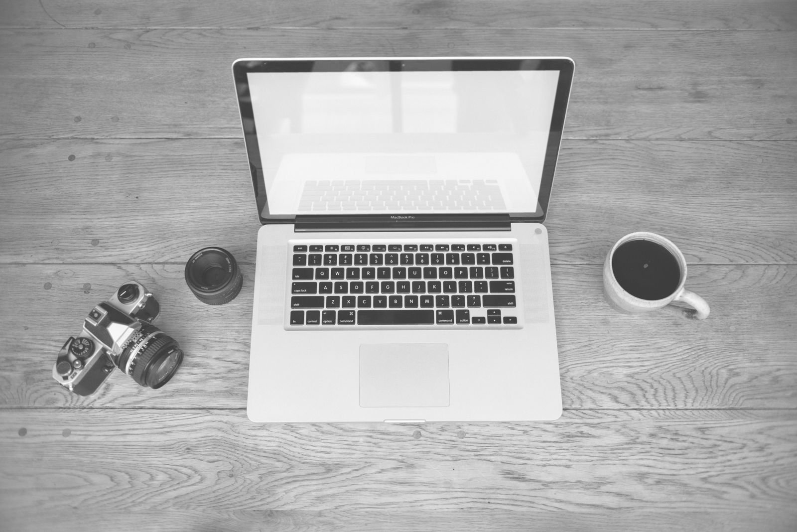 A laptop, camera and coffee cup on a wooden desk