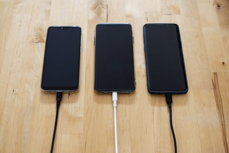 Three smartphones connected to chargers on a wooden surface